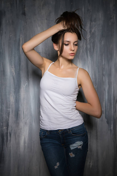 Portrait of seductive brunette wearing casual clothes and posing near grey wall - 写真・画像