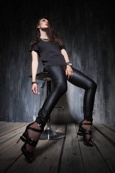 Sexy mujer joven vestida con ropa negra de moda sentada en la silla y mirando hacia arriba
 - Foto, imagen