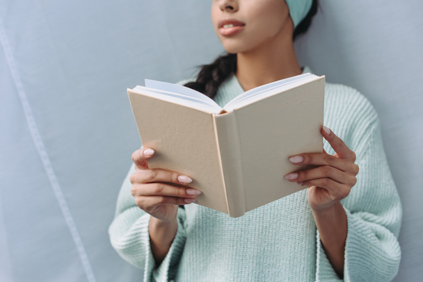 körülvágott kép kevert lány türkizkék pulóver és a gazdaság könyv otthon fejpánt - Fotó, kép