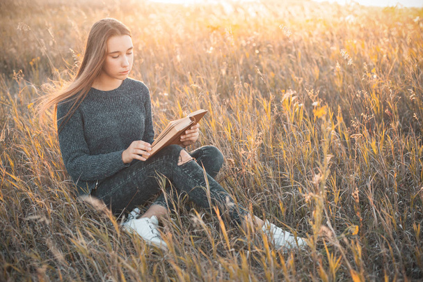 Νεαρή γυναίκα διαβάζοντας ένα βιβλίο σε εξωτερικούς χώρους στο ηλιοβασίλεμα - Φωτογραφία, εικόνα