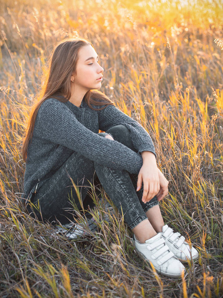 Beautiful young woman sitting in high grass at sunset - Foto, afbeelding