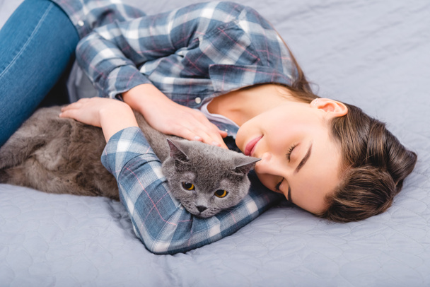 νεαρή γυναίκα ξαπλωμένη στο κρεβάτι με αξιολάτρευτο γκρίζα γάτα - Φωτογραφία, εικόνα