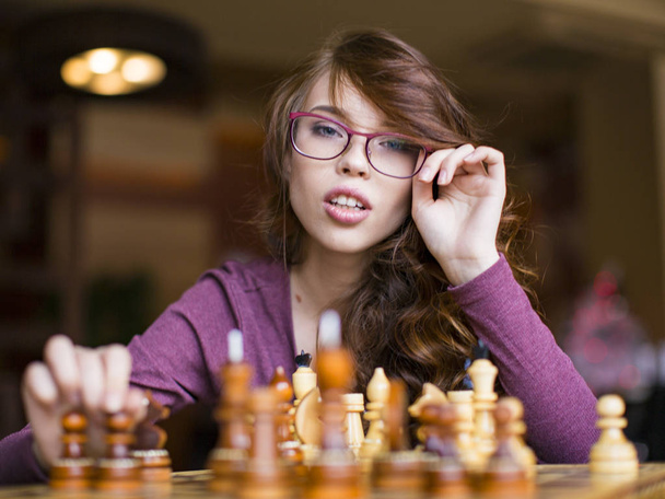 メガネはチェスのゲームをプレイで女性のクローズ アップ。カメラを見て - 写真・画像