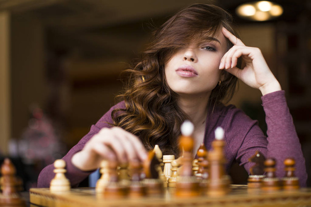 Jovem mulher branca inteligente jogando xadrez em casa vestindo roupas casuais inteligentes
 - Foto, Imagem