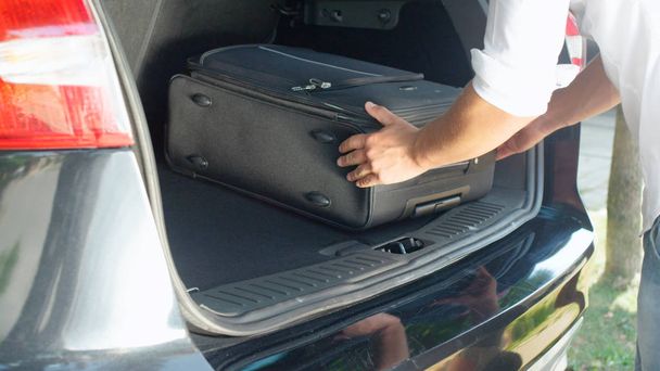 クローズ アップ: 認識できない男は休日に行く前に広々 とした車のトランクに彼の旅行バッグを入れてします。大型の黒い Suv の後部コンパートメントに彼の荷物を梱包若い男性旅行者. - 写真・画像