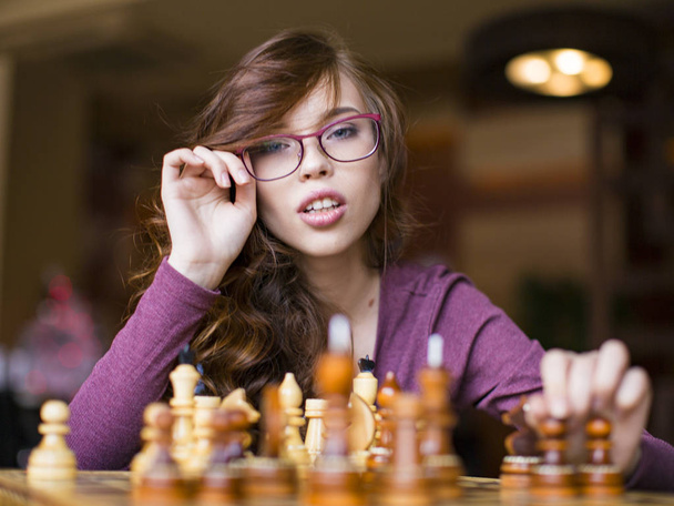 Όμορφη μελαχρινή γυναίκα με γυαλιά που παίζουν σκάκι. Εσωτερικη πορτρέτο, celective εστίαση. - Φωτογραφία, εικόνα