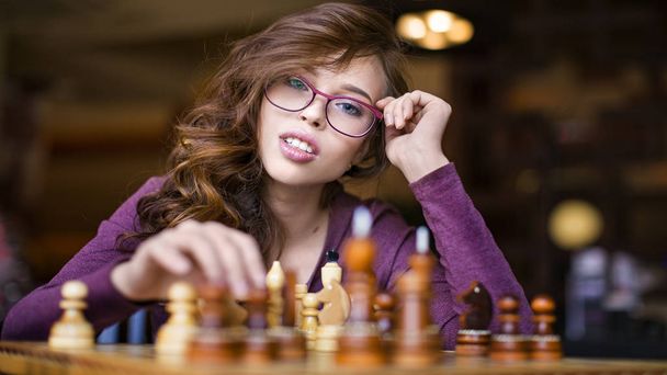 Nuori älykäs valkoihoinen nainen pelaa shakkia kotona yllään älykäs rento vaatteita
 - Valokuva, kuva