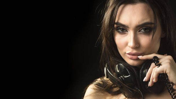 Retrato de cerca de una joven hermosa morena sosteniendo auriculares sobre fondo gris oscuro
 - Foto, Imagen