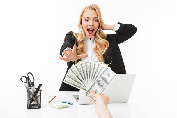 Portrait of successful woman wearing office clothing grabbing dollar bills at workplace isolated over white background - Foto, imagen