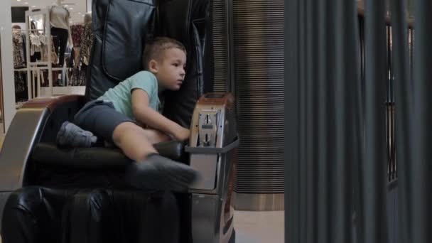 ein gelangweilter Junge im Massagesessel im Einkaufszentrum - Filmmaterial, Video