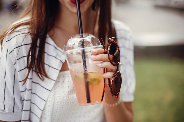 Ban single use plastic. Happy hipster girl  in retro dress, holding plastic cup and straw. Beautiful stylish young woman holding cold drink and relaxing in city street. - Photo, Image