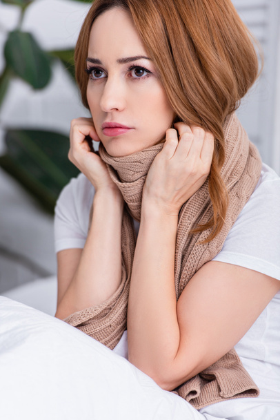 portrait of sick woman with makeup and scarf sitting on bed at home - Foto, Bild