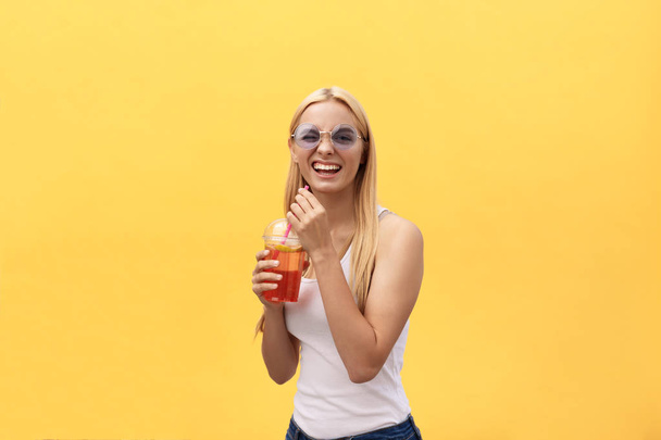 Skvělé žena v sluneční brýle nosit bílé tričko držte sklenici šťávy na žlutém pozadí, samostatný - Fotografie, Obrázek