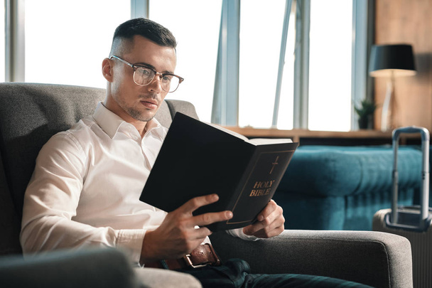 Tmavovlasý muž nosí brýle drží Holy Bible - Fotografie, Obrázek