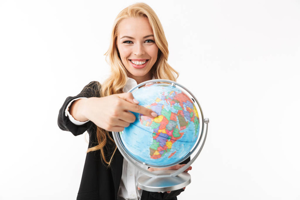 Portrait of a pretty smiling young businesswoman standing isolated over white background, holding earth globe, pointing finger - Foto, imagen