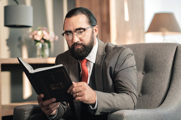 Dark-haired man enjoying his time while reading the Bible - Foto, afbeelding