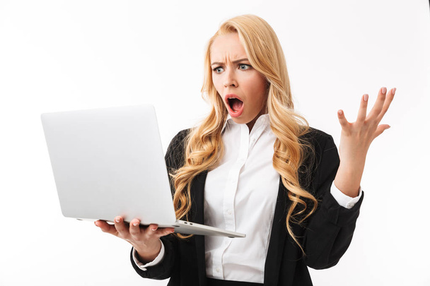 Photo of shocked businesswoman wearing office suit holding silver laptop isolated over white background in studio - Foto, afbeelding