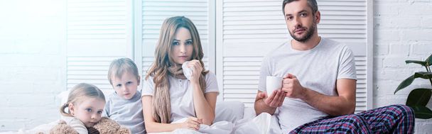 vista panorámica del marido dando taza de té a la esposa enferma, los niños mirando a la cámara en el dormitorio
 - Foto, imagen