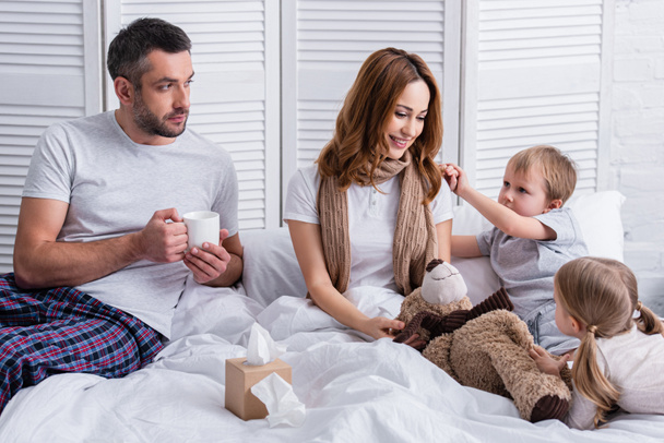 husband and children supporting smiling sick mother in bedroom - Photo, Image