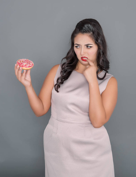 Krásné plus velikost ženy při pohledu na donut s pochybností. Nadváhou koncepce - Fotografie, Obrázek