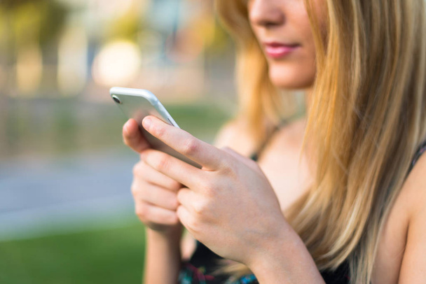 Красивая молодая девушка-подросток в парке отправляет сообщение или электронную почту с мобильного телефона
 - Фото, изображение