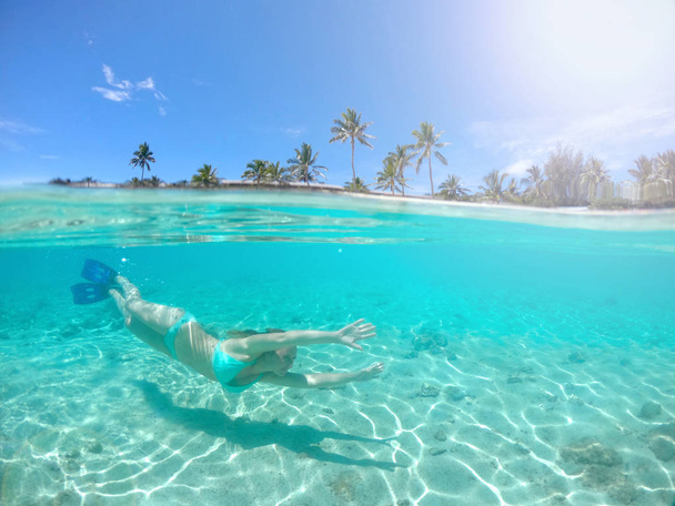 HALF UNDERWATER: Young female traveler diving in the tranquil crystal clear water along the sandy shore of spectacular tropical island. Caucasian woman having fun swimming in the refreshing water. - Foto, imagen