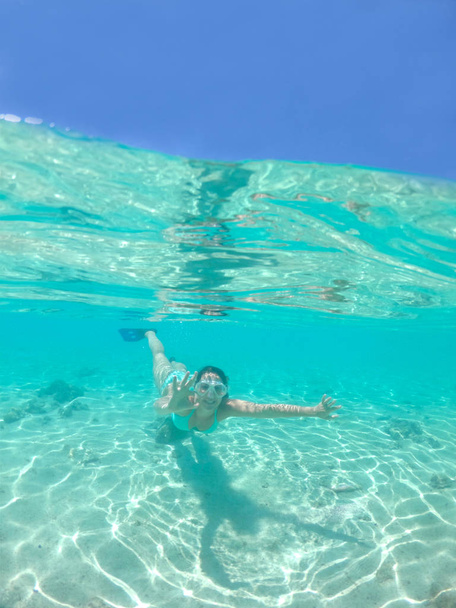 HALF UNDERWATER: Iloinen nuori nainen tekee käsi ele kun snorklaus lähellä näyttäviä Cook Islands. Sopii tyttö turkoosi bikinit sukellus henkeäsalpaava lasillinen vesillä Tyynenmeren
. - Valokuva, kuva