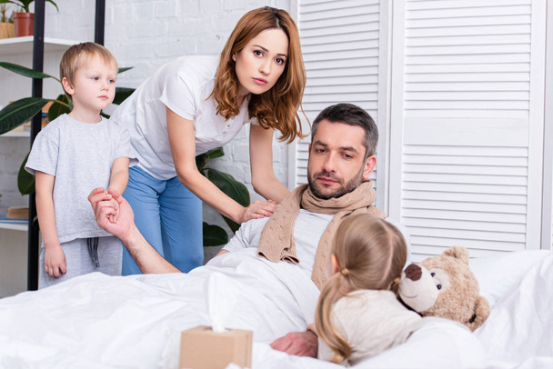 wife and children taking care of sick father in bedroom - Фото, зображення