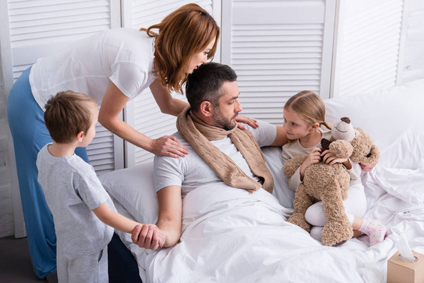 korkea kulma näkymä vaimo ja lapset huolehtivat sairas isä makuuhuoneessa
 - Valokuva, kuva