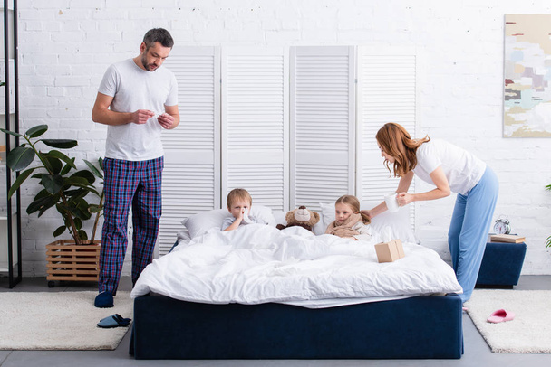 parents taking care of sick children in bedroom - Foto, Bild