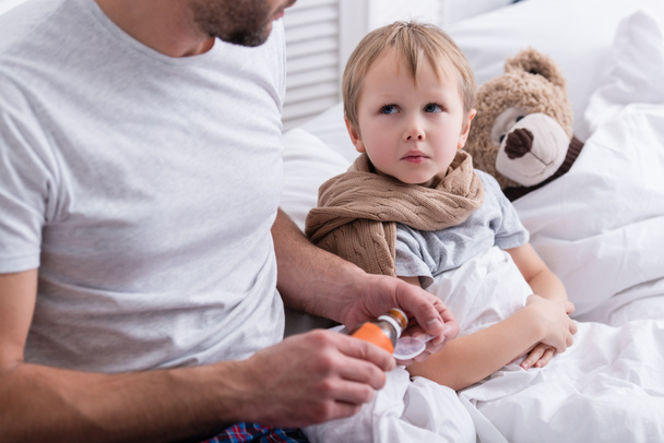 cropped image of dad taking care of sick son in bedroom and pouring medicines in spoon - Photo, Image
