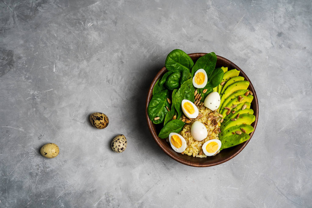 Top view of salad with bulgur, spinach, avocado and quail eggs in wooden bowl on concrete background - Valokuva, kuva