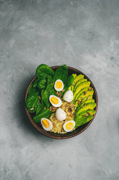 Top view of salad with bulgur, spinach, avocado and quail eggs in wooden bowl on concrete background - Fotoğraf, Görsel