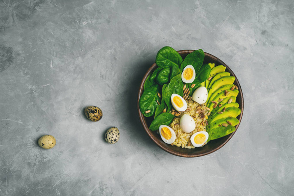 Fresh vegetarian salad with bulgur, spinach, avocado and quail eggs in wooden bowl on concrete background - Photo, image