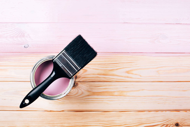 Open can of pink paint with white brush on painting wooden board. - Foto, afbeelding