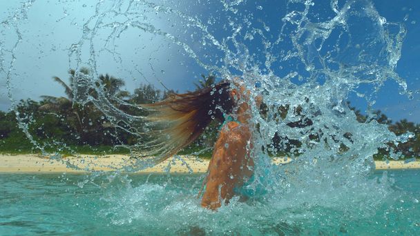Nahaufnahme: Glasige Tropfen Meerwasser fliegen in die Luft, nachdem ein kaukasisches Mädchen im türkisfarbenen Bikini ihre Haare zurückwirft. junge Reisende spielt mit ihren Haaren im erfrischenden kristallklaren Pazifik. - Foto, Bild