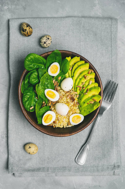Top view of green salad with bulgur, spinach, avocado and quail eggs in wooden bowl - 写真・画像