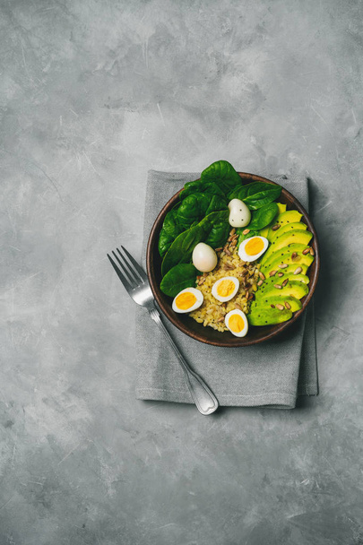 Top view of green salad with bulgur, spinach, avocado and quail eggs in wooden bowl on concrete background - Photo, image