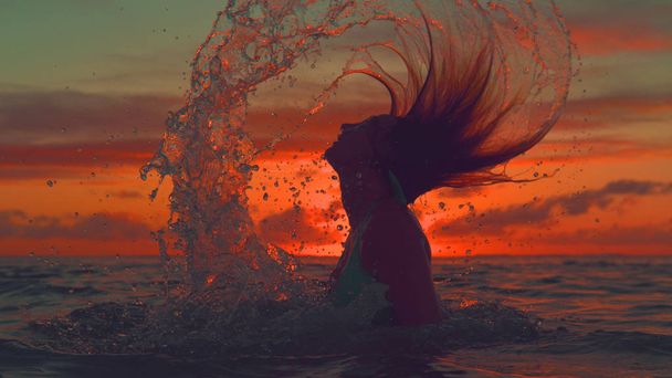 Nahaufnahme, Silhouette: Unerkennbares Mädchen erhebt sich aus dem kühlen Ozean und peitscht den Kopf bei herrlichem Sommersonnenaufgang zurück. malerische Aufnahme einer verspielten Reisenden im Bikini, die im Wasser plantscht. - Foto, Bild