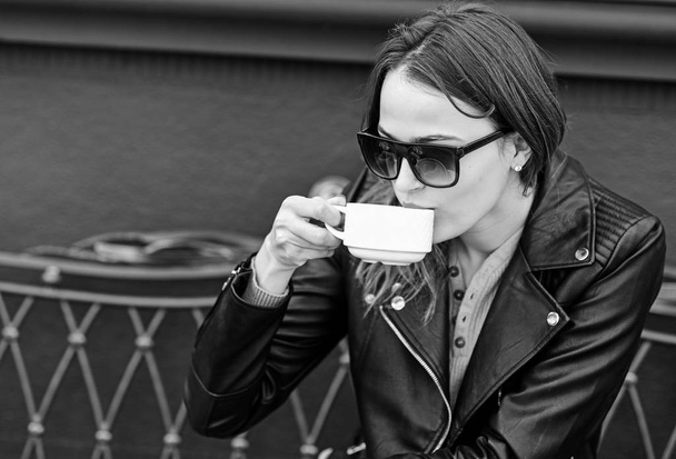 Girl in sunglasses drinks tasty coffee on brown terrace background - 写真・画像