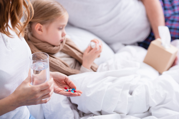cropped image of parents taking care of sick daughter in bedroom, giving her pills and glass of water - Foto, Imagen