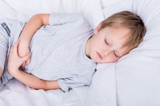 sick boy lying on bed and touching painful stomach in bedroom - Zdjęcie, obraz