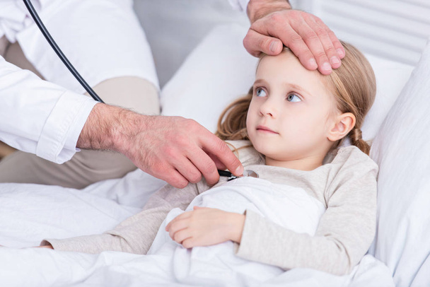 cropped image of pediatrist in white coat examining sick kid with stethoscope at home - Foto, Imagem