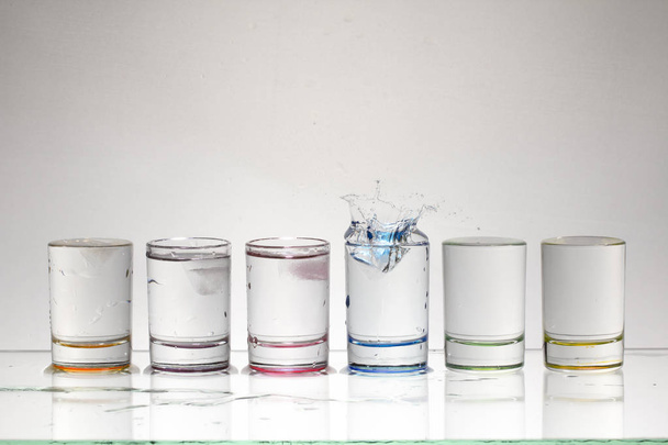 Kropelki wody z upuszczanie kostkę lodu do szklanki płynu. Z bliska - Zdjęcie, obraz