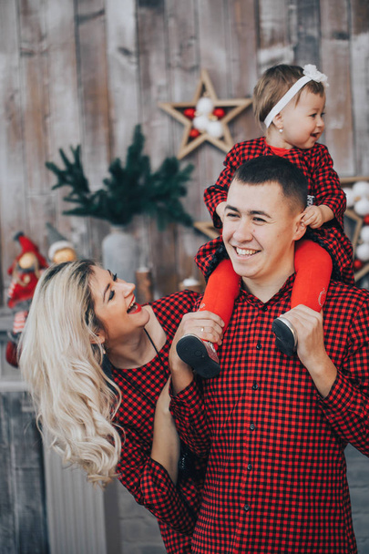 Familia feliz con su hija pequeña juntos en la habitación de vacaciones decoradas con un árbol de Navidad y una corona en el fondo
 - Foto, Imagen