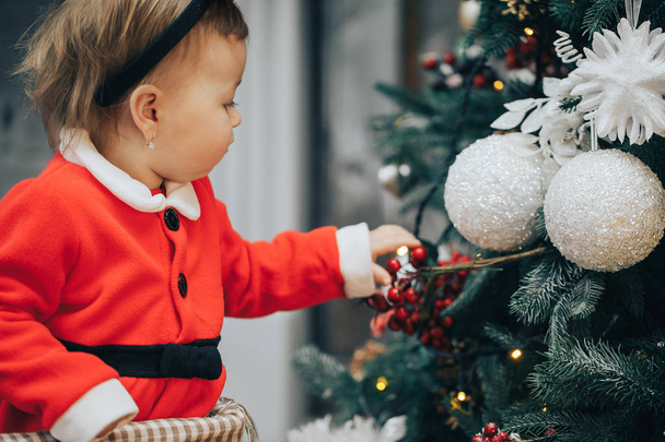 Urlaub, Weihnachten und Menschen-Konzept - junges glückliches Baby-Mädchen im Weihnachtsanzug mit Funkeln auf Hintergrund mit Kopierraum - Foto, Bild