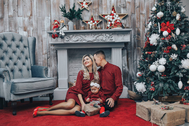 Ευτυχισμένη οικογένεια με την μικρή κόρη του μαζί σε διακοπές διακοσμημένα δωμάτιο με ένα χριστουγεννιάτικο δέντρο και ένα στεφάνι στο φόντο - Φωτογραφία, εικόνα