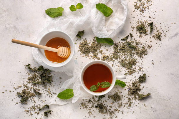 Taza de té caliente con menta seca y miel en mesa ligera
 - Foto, imagen