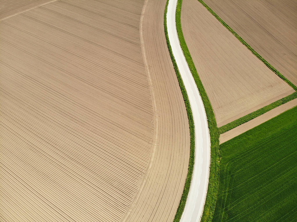 AERIAL: Espectacular camino rural vacío que pasa por vastos campos arados y pastizales en un soleado día de verano. Volando por encima de una ruta de hormigón que atraviesa un paisaje. Impresionante naturaleza
. - Foto, Imagen