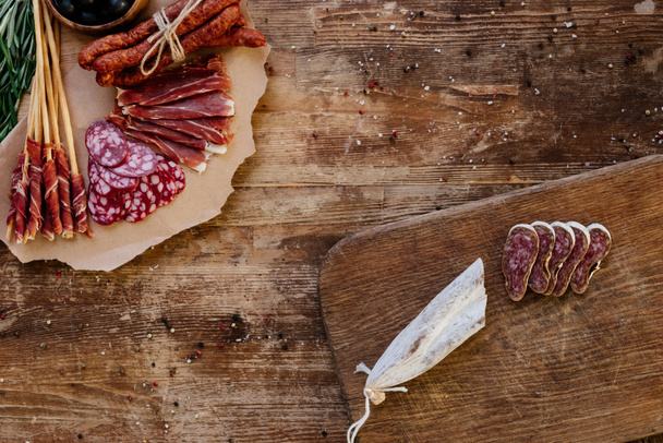 top view of cutting boards with sliced prosciutto, salami and smoked sausages on wooden table  with scattered spices - Photo, Image